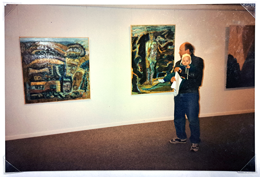 Seppo Kääriäinen, sylissään Antti. 1989. Taustalla maalaukset "Shamaani" ja "Vapautuminen". Kuva Irma Kääriäinen.